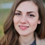 Close-up portrait of a smiling woman with freckles and long hair in a Budapest park during fall.